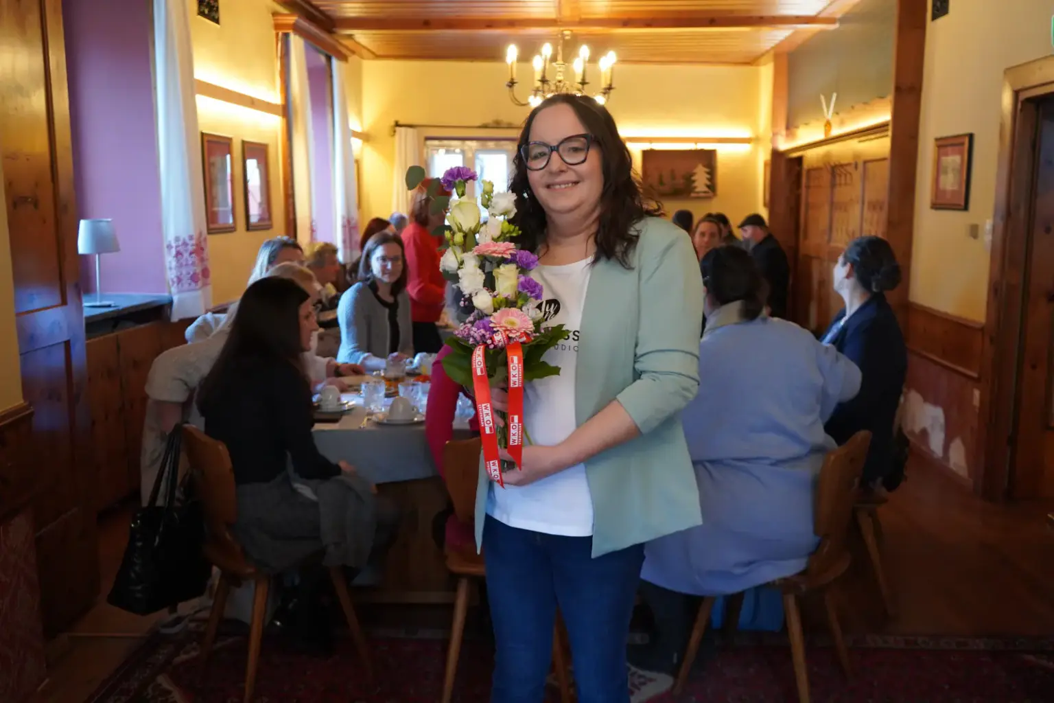 JuNe Design Studio in St. Michael feierte 10-jähriges Jubiläum Eine Frau steht im Raum mit Blumen in der Hand, im Hintergrund sind ihre Gäste beim Frühstücken.