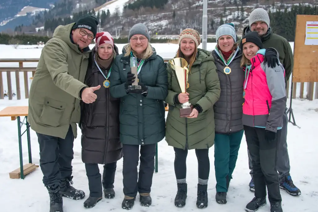 Fünf Frauen und zwei Männer mit einem Pokal und Medaillen auf einer Eisbahn