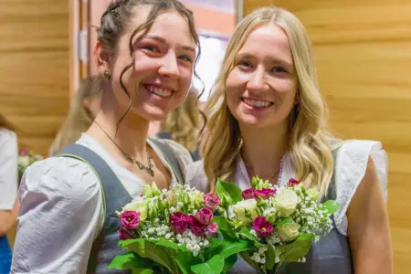 Zwei junge Damen in Dirndlkleidern mit Blumensträußen