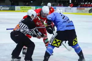 Zwei Eishockeyspieler stehen sich auf dem Eis gegenüber, daneben steht der Schiedsrichter.