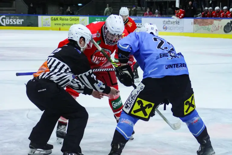 Zwei Eishockeyspieler stehen sich auf dem Eis gegenüber, daneben steht der Schiedsrichter.