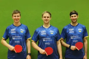 Drei junge Männer vor einer grünen Wand mit je einem Tischtennisschläger in der Hand.