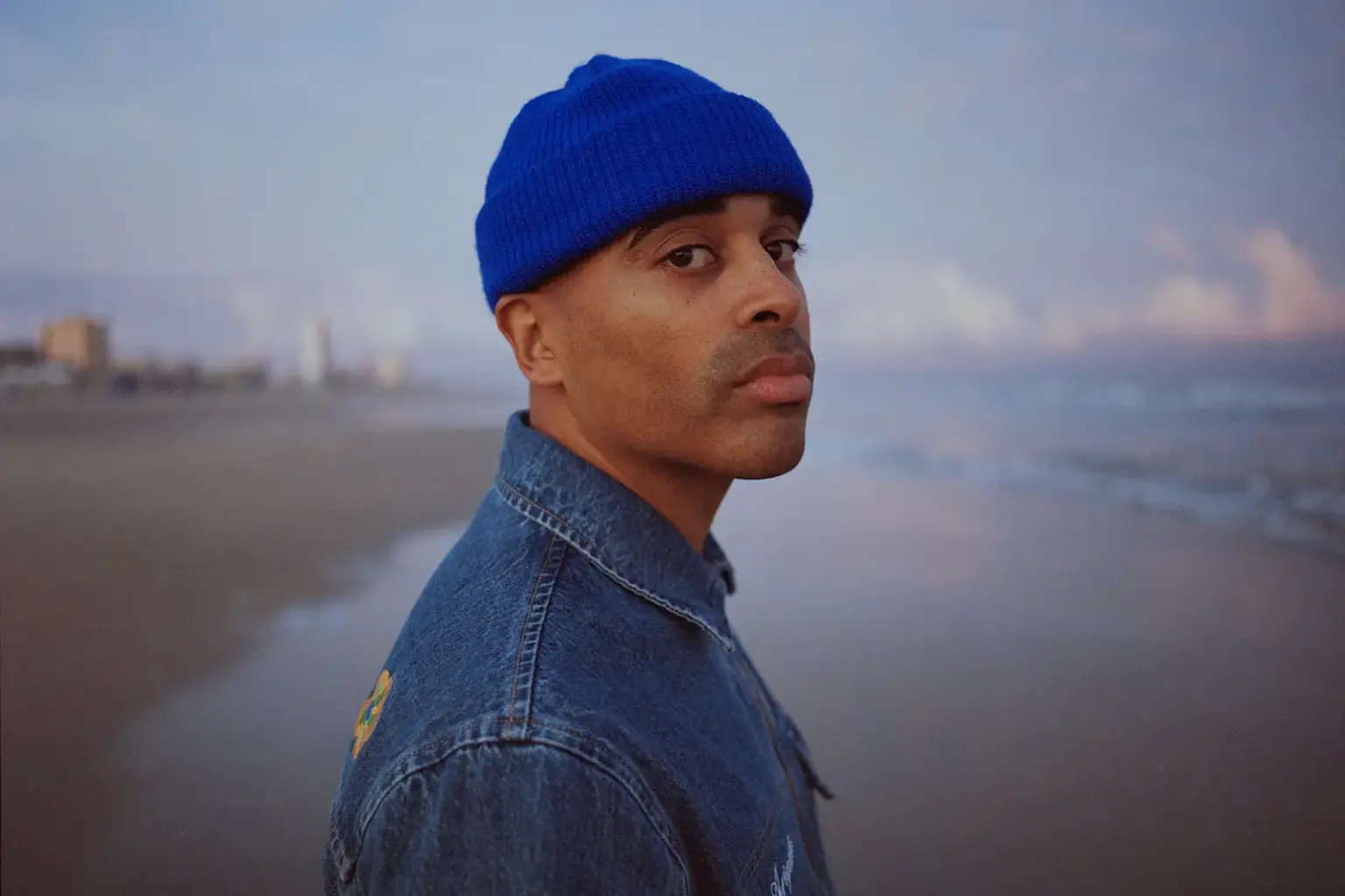 Ein Mann mit Jeansjacke und blauer Mütze an einem Strand