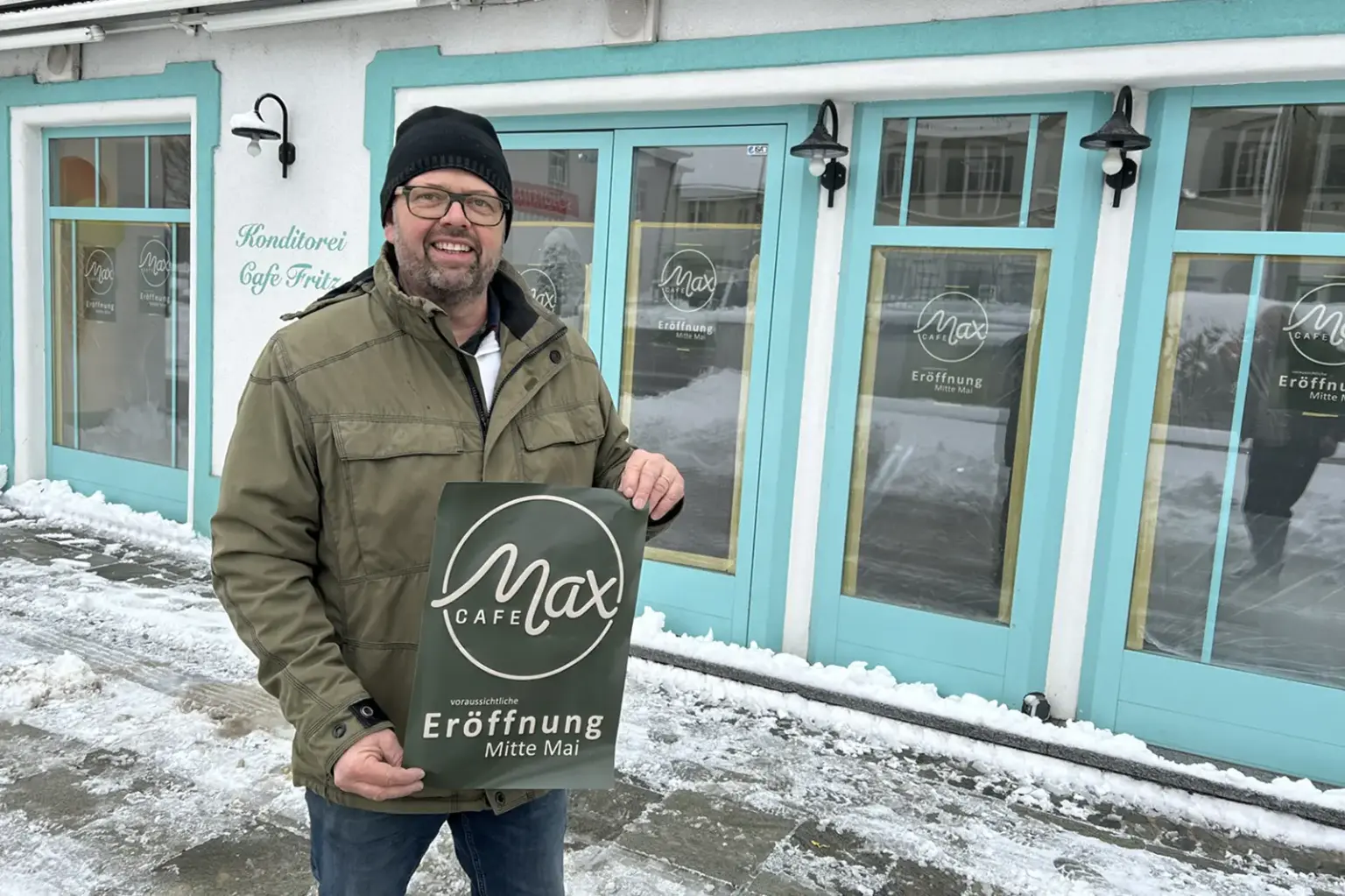 Ein Mann mit einem Plakat in der Hand vor einem Geschäftslokal.
