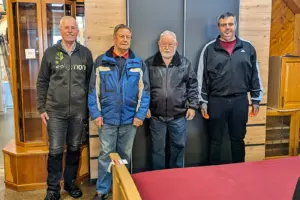 Vier ältere Männer vor einer Holzwand