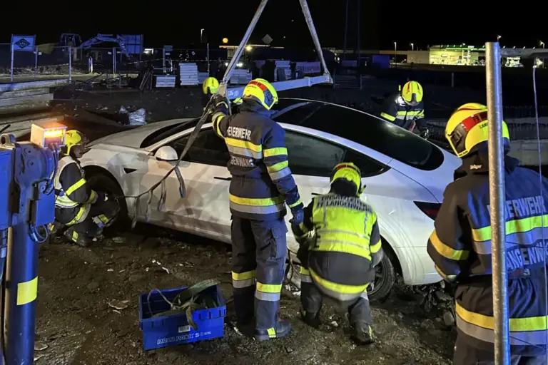 Fahrzeugbergung aus der Baustelle Mehrere Feuerwehrmänner befestigen ein Auto an einem Kran