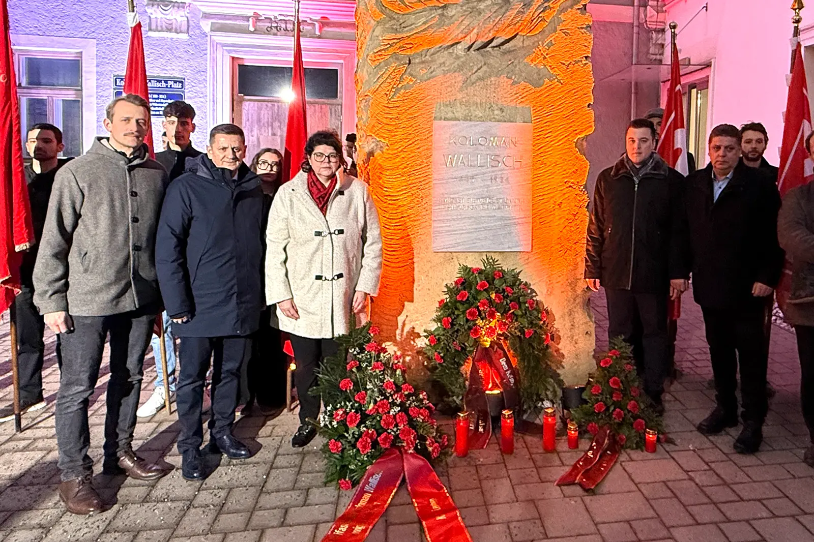 Mehrere Personen vor einem Denkmal mit Kränzen