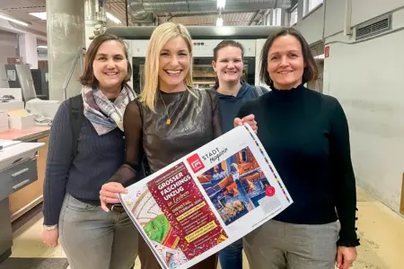 Vier lächelnde Frauen mit einer Zeitungsdoppelseite in einer Druckerei