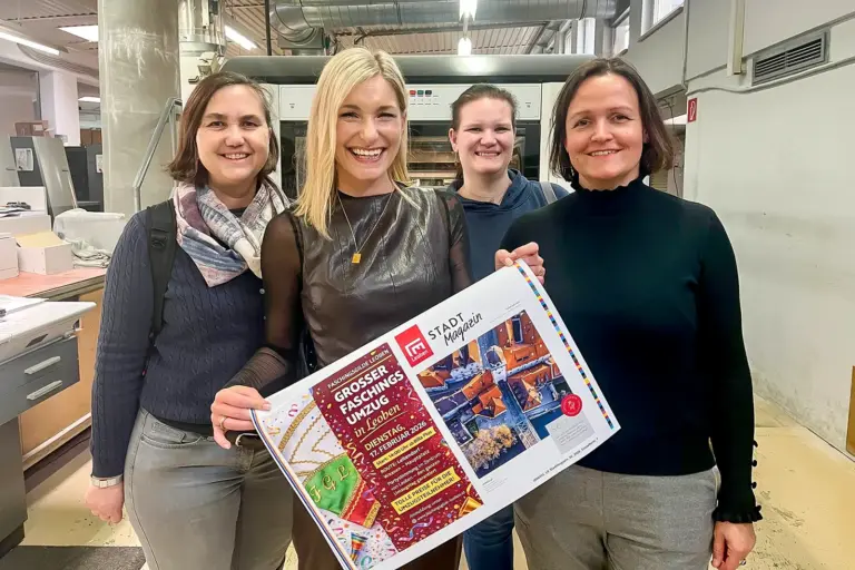 Vier lächelnde Frauen mit einer Zeitungsdoppelseite in einer Druckerei