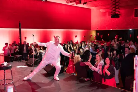 Galanacht zum Valentinstag in Leoben Ein Mann im weißen Anzug auf einer Bühne vor vielen ZuschauerInnen