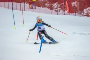 Ein kleines Mädchen auf Schi fährt durch Slalomstangen.