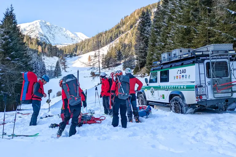 Gemeinsame Einsatzübung der Bergrettung Mehrere Personen mit großen Rucksäcken stehen im Schnee, daneben sind Schi und Stöcke sowie ein Auto der Bergrettung zu erkennen.