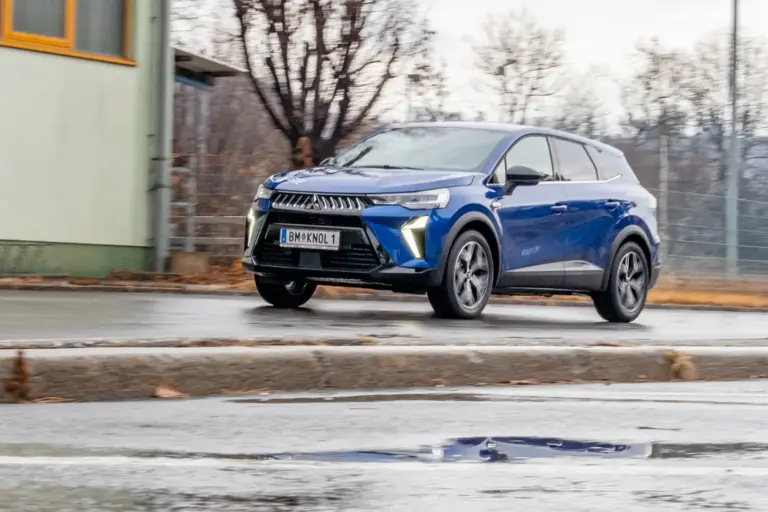 Ein blau lackiertes Auto der Marke Mitsubishi fährt von rechts nach links