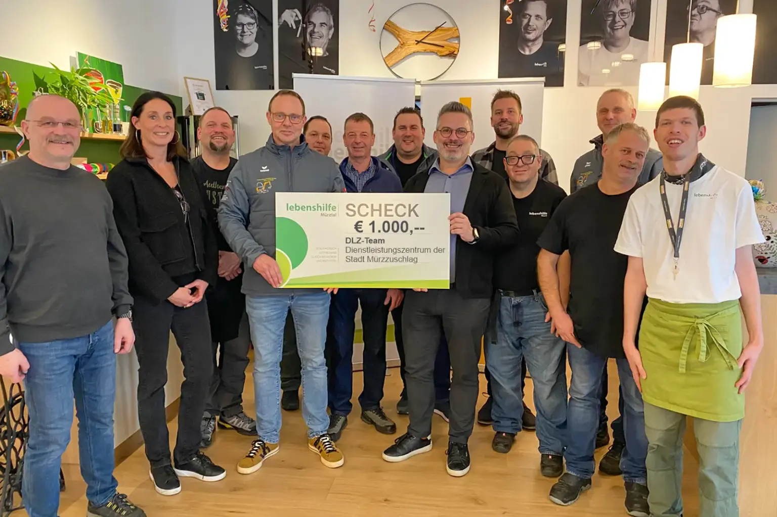 Erlös des Adventmarkts gespendet Zahlreiche Menschen stehen in einem Raum, in der Mitte wird gemeinsam ein großer Scheck gehalten.