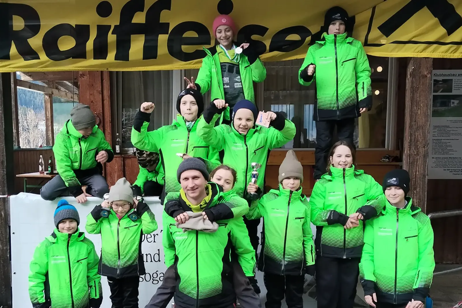 Ein Gruppe von jungen Menschen in Schianzügen mit Medaillen und Pokalen in der Hand.