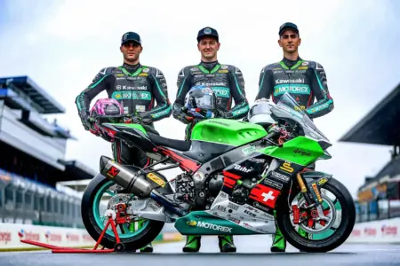 Ungewisse Situation für Brucker Rennfahrer Drei Männer mit Kappe auf dem Kopf und in Motorrad-Rennanzügen. Davor steht ein Motorrad.