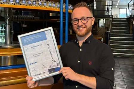 Ein Mann mit Brille vor einer Biertheke präsentiert eine Urkunde