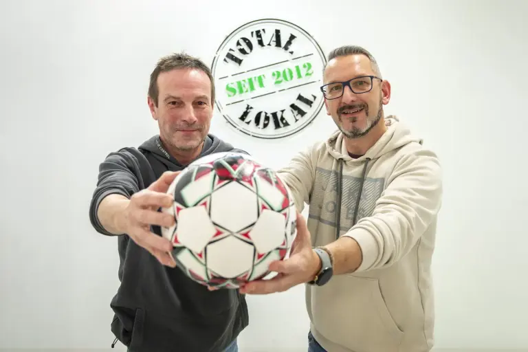 Fußball-Unterhaus zieht bei der Rundschau ein Zwei Männer halten gemeinsam einen Fußball in den Händen.
