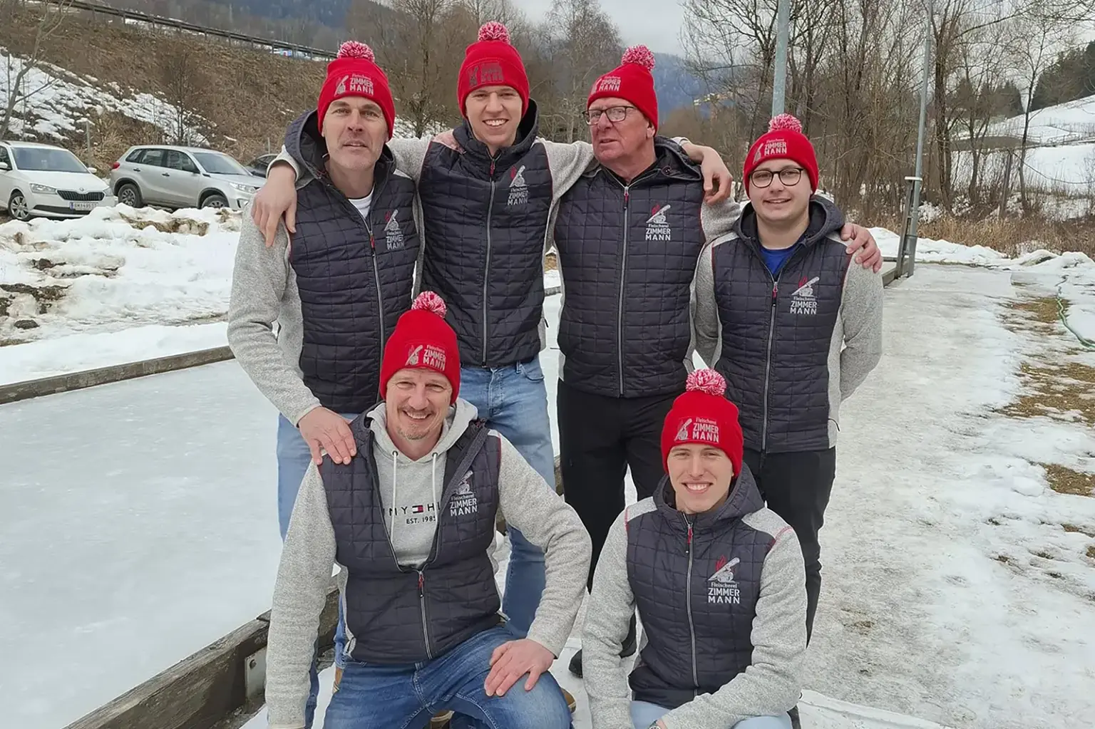 Teilnehmerrekord beim Spitaler Gemeindepokal Sechs Männer stehen vor einer Eisbahn, alle sechs haben die selbe graue Jacke und rote Haube auf.