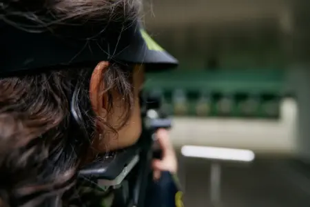 Eine Sportschützin ist seitlich von hinten zu sehen, sie zielt mit dem Gewehr in Richtung Zielscheiben.