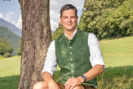 Ein Mann mit Trachtengewand sitzt vor einem Baum.