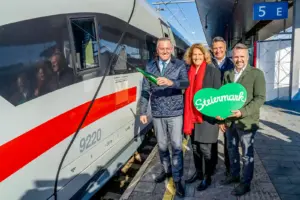 Eine Frau und drei Männer neben einer stehenden Schnellzuggarnitur.