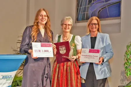 Drei festlich gekleidete Frauen bei einer Preisverleihung mit Urkunden und einer Trophäe in Form einer Keramikskulptur in Händen