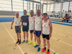Fünf Männer stehen nebeneinander in einer Leichtathletik-Halle.