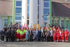 Eine große Gruppe von Personen in festlicher Kleidung mit Fahnen vor einem Gebäude