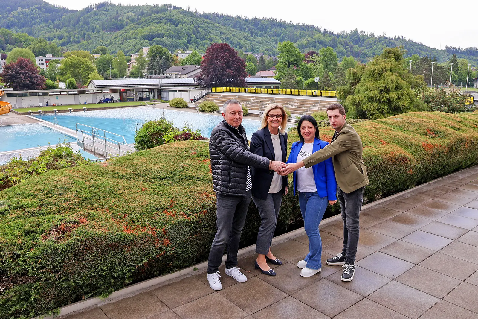 Zwei Männer und zwei Frauen reichen sich vor einem großen Wasserbecken die Hände