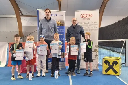 Sechs Kinder mit Urkunden und Pokalen, dahinter stehen zwei Männer. Alle befinden sich in einer Tennishalle.