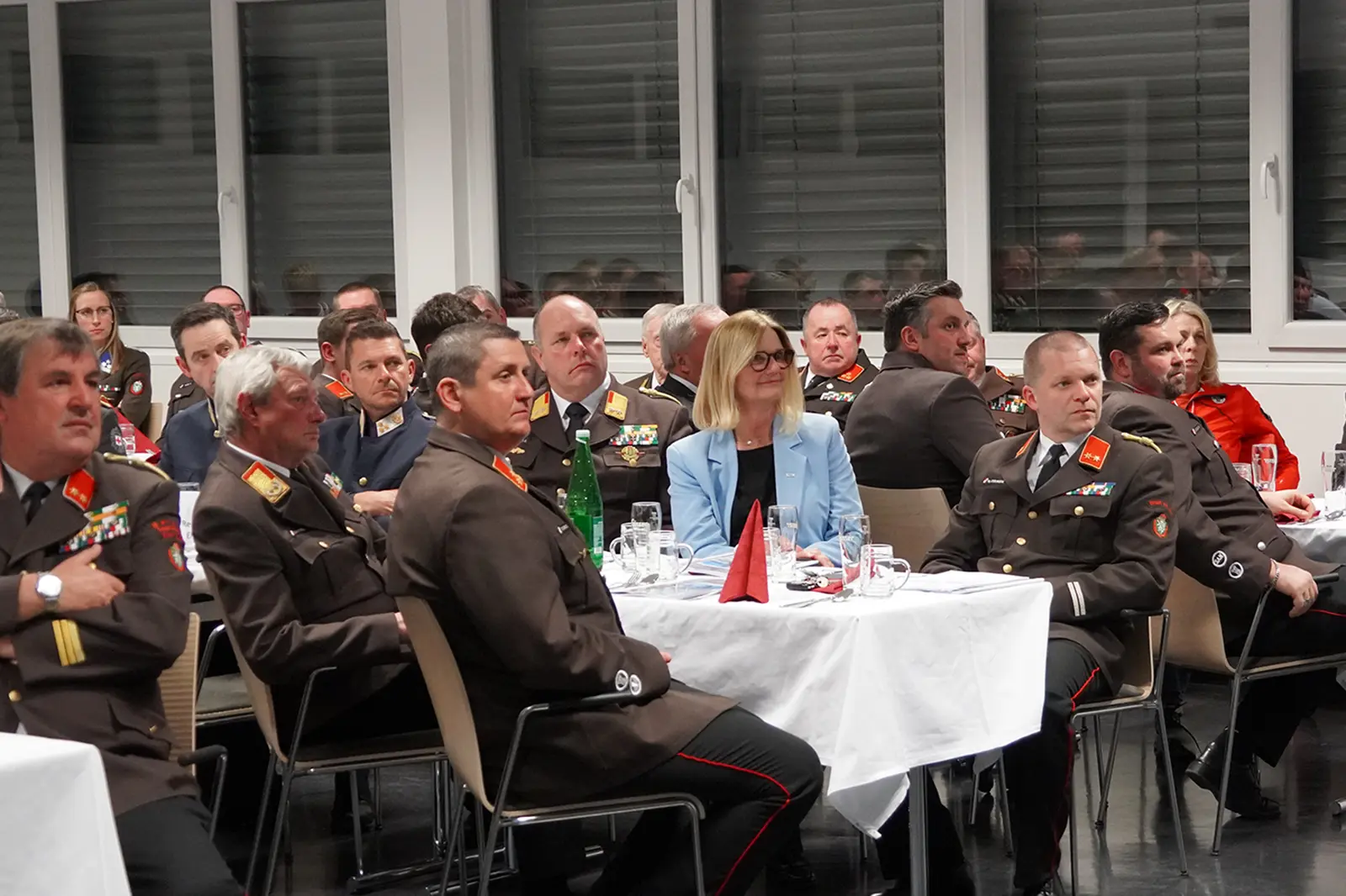 Mehrere Personen, zum Teil in Uniform sitzen an gedeckten Tischen