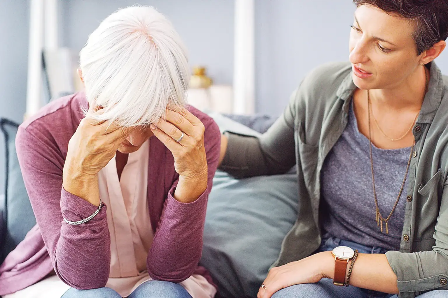 Eine ältere Frau mit weißen Haaren vergräbt ihr Gesicht in den Händen, eine jüngere Frau sitzt tröstend daneben