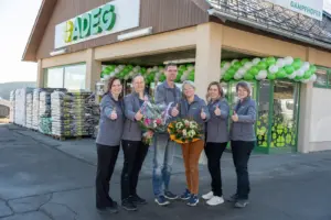 Fünf Frauen und ein Mann mit Blumensträußen vor einem Adeg-Geschäft