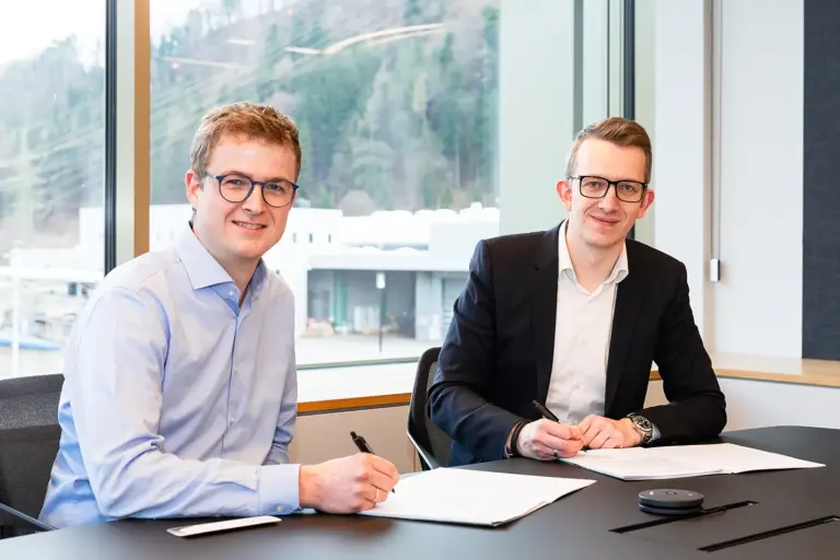 Zwei Männer sitzen an einem Tisch und unterzeichnen Papiere