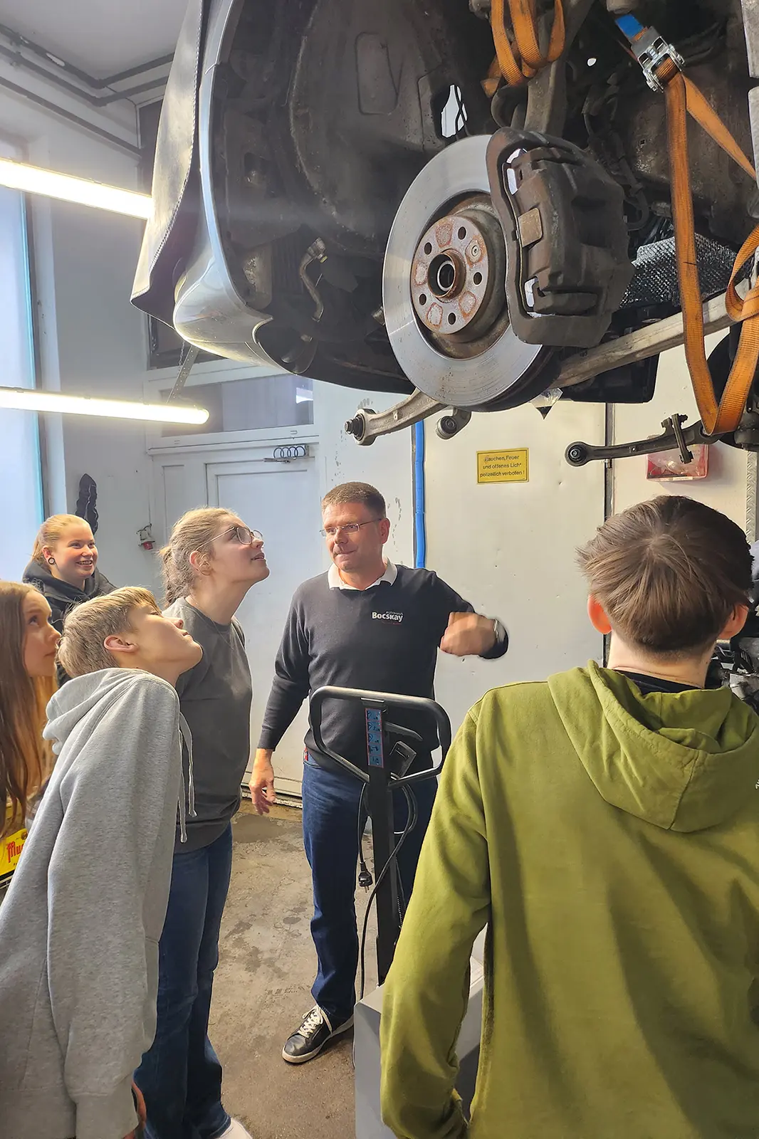 Mehrere Jugendliche stehen unter einem Auto auf einer Hebebühne