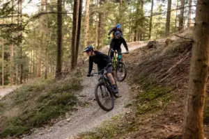 Drei Mountainbiker auf einer als Trail mit Steilkurven ausgebauten Abfahrt durch einen Wald