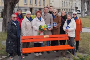 Eine Gruppe von Personen stehen hinter einer orangen Parkbank