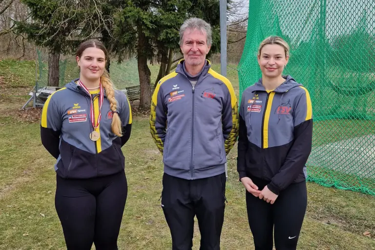 Zwei Damen und ein Mann stehen nebeneinander im Freien.