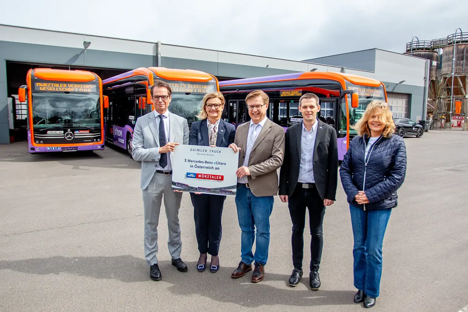 Zwei Frauen und drei Männer stehen vor drei in Orange und Lila lackierten Linienbusse