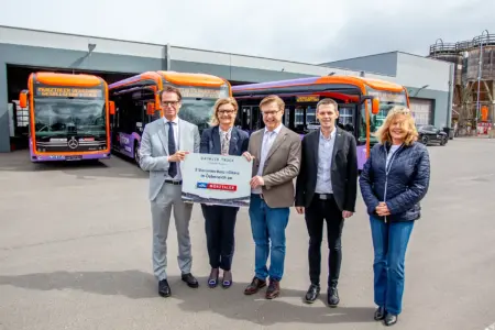 Zwei Frauen und drei Männer stehen vor drei in Orange und Lila lackierten Linienbusse