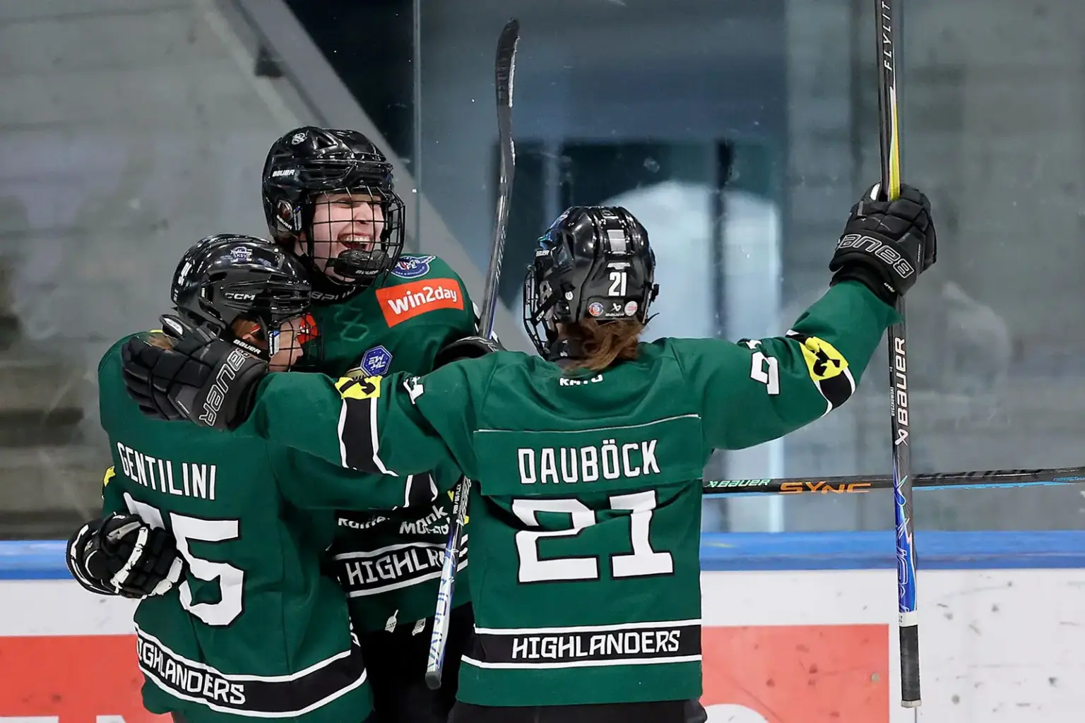 Drei Eishockeyspielerinnen jubeln gemeinsam in eine Eishalle.