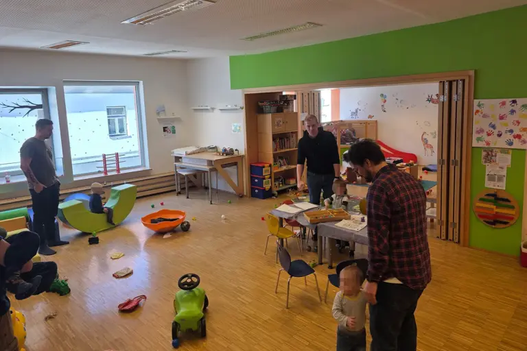 Drei Männer spielen mit kleinen Kindern in einem großen Raum