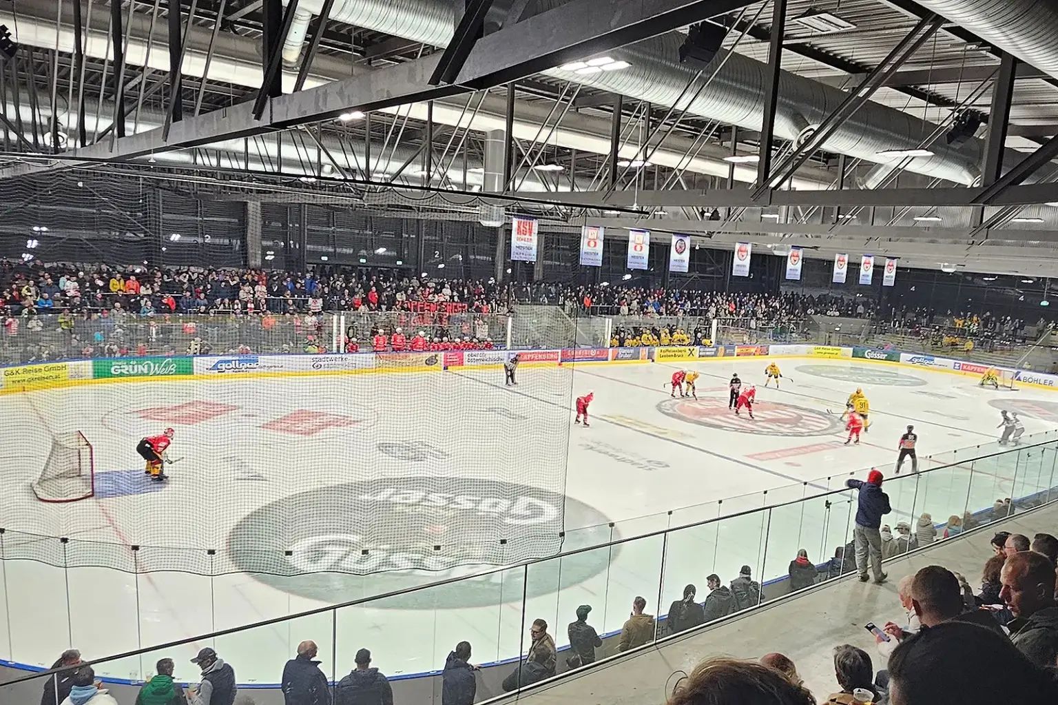 Eine Eishalle mit zahlreichen Zusehern und Eishockeyspielern auf dem Eis.