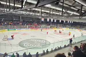 Eine Eishalle mit zahlreichen Zusehern und Eishockeyspielern auf dem Eis.