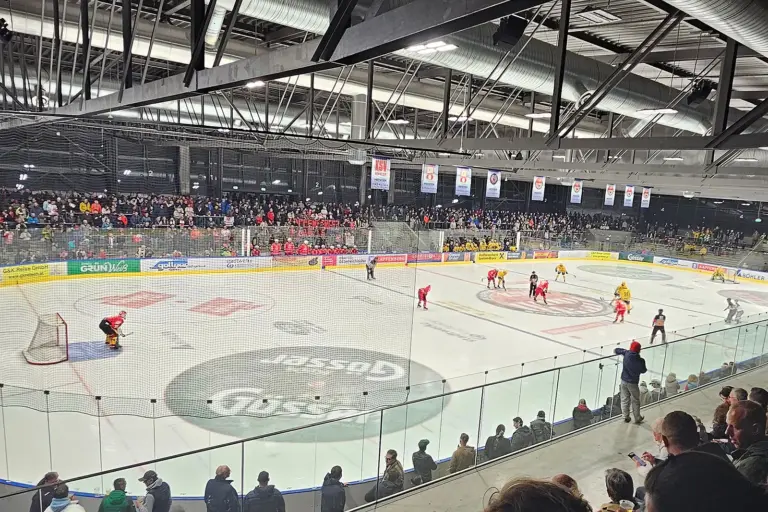 Eine Eishalle mit zahlreichen Zusehern und Eishockeyspielern auf dem Eis.