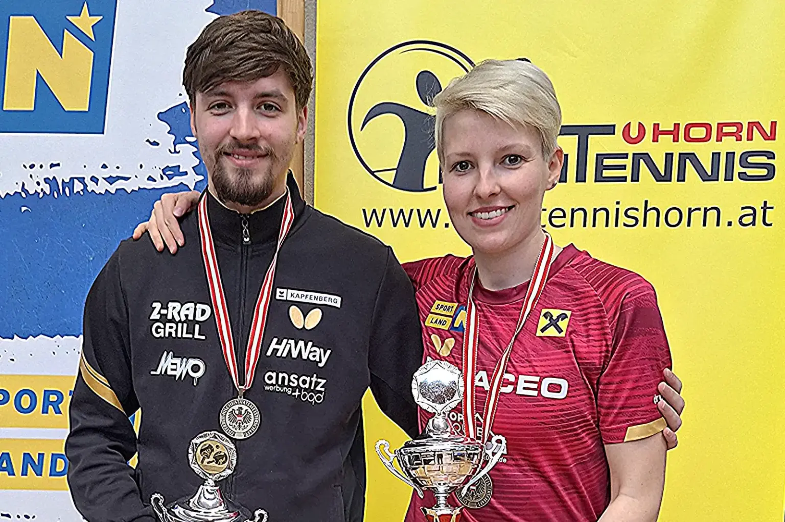 Ein Mann und eine Frau stehen nebeneinander mit je einem Pokal in der Hand.