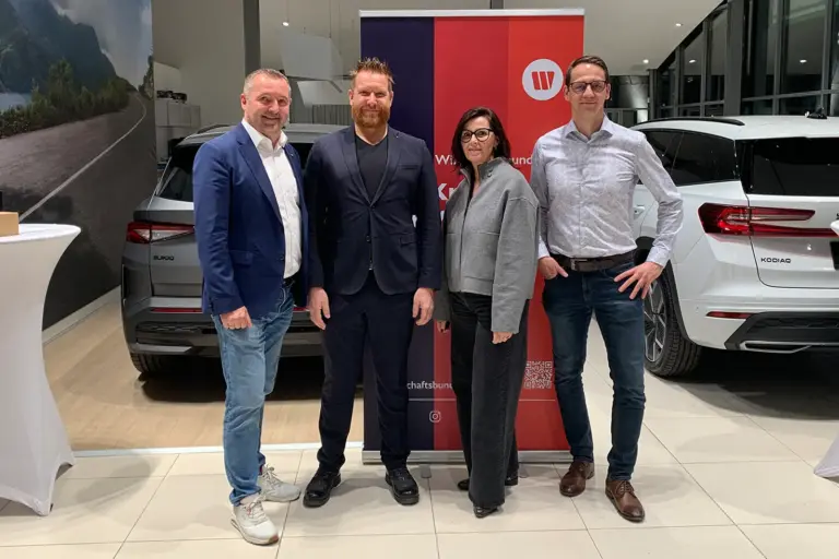 Drei Männer und eine Frau stehen im Schauraum eines Autohauses