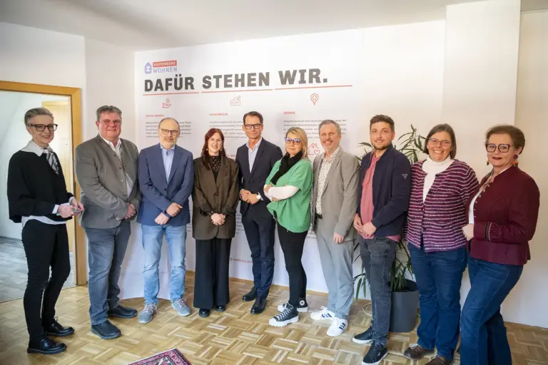 Eine Gruppe von Menschen stehen nebeneinander vor einer Wand.