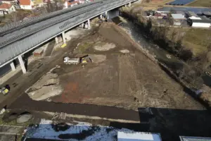 Ein großer Platz mit Erde von oben. Links ist eine Straße und rechts ein Fluss erkennbar.